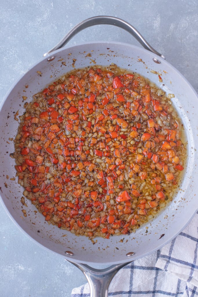 Onions, garlic, red peppers in a pan for breakfast casserole with bacon on a grey background