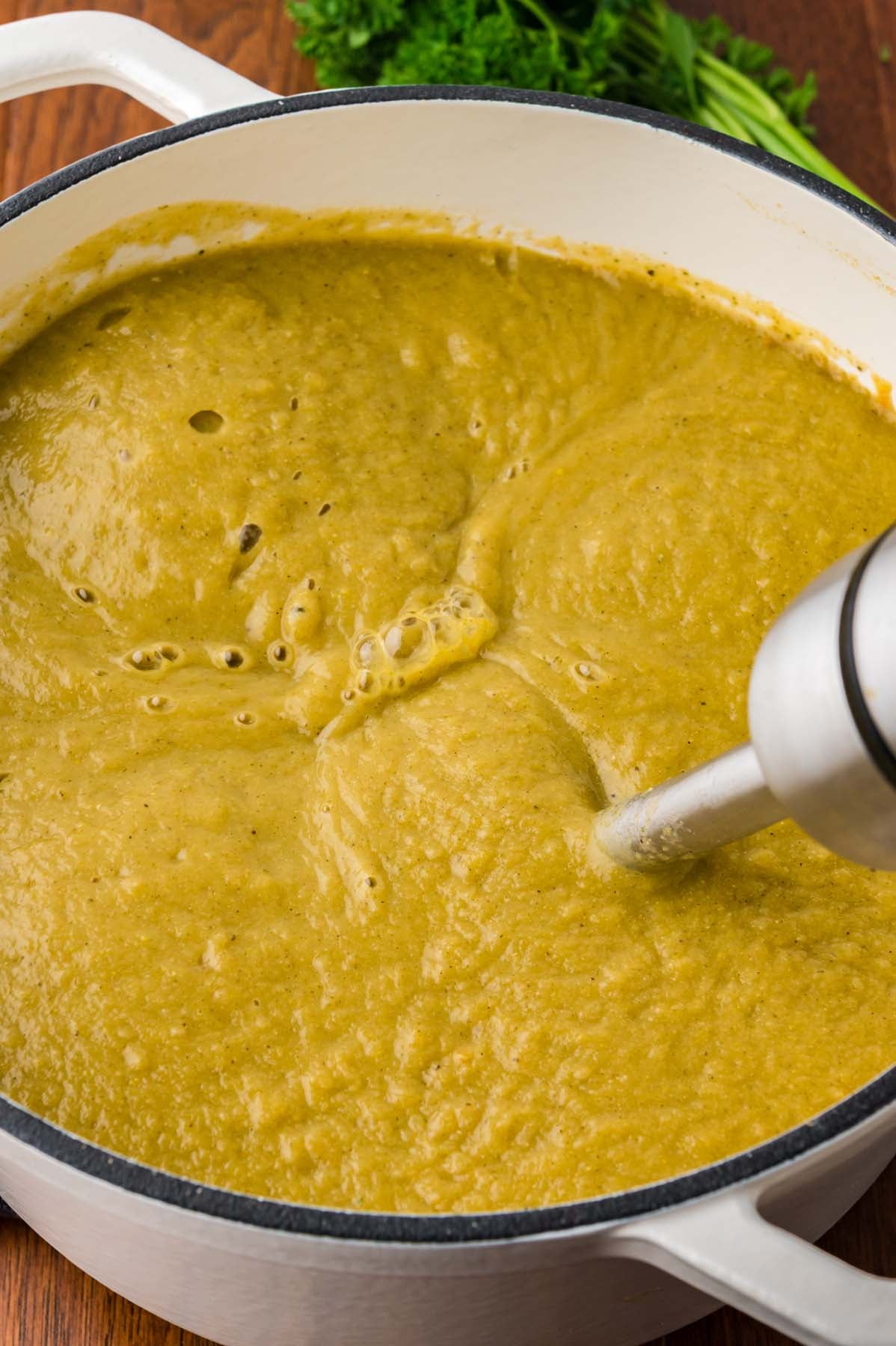 Creamy vegetable soup in a dutch oven being blended with an immersion blender
