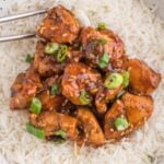 A white bowl of white rice topped with healthy ginger chicken with green onions on top and chopsticks on the side