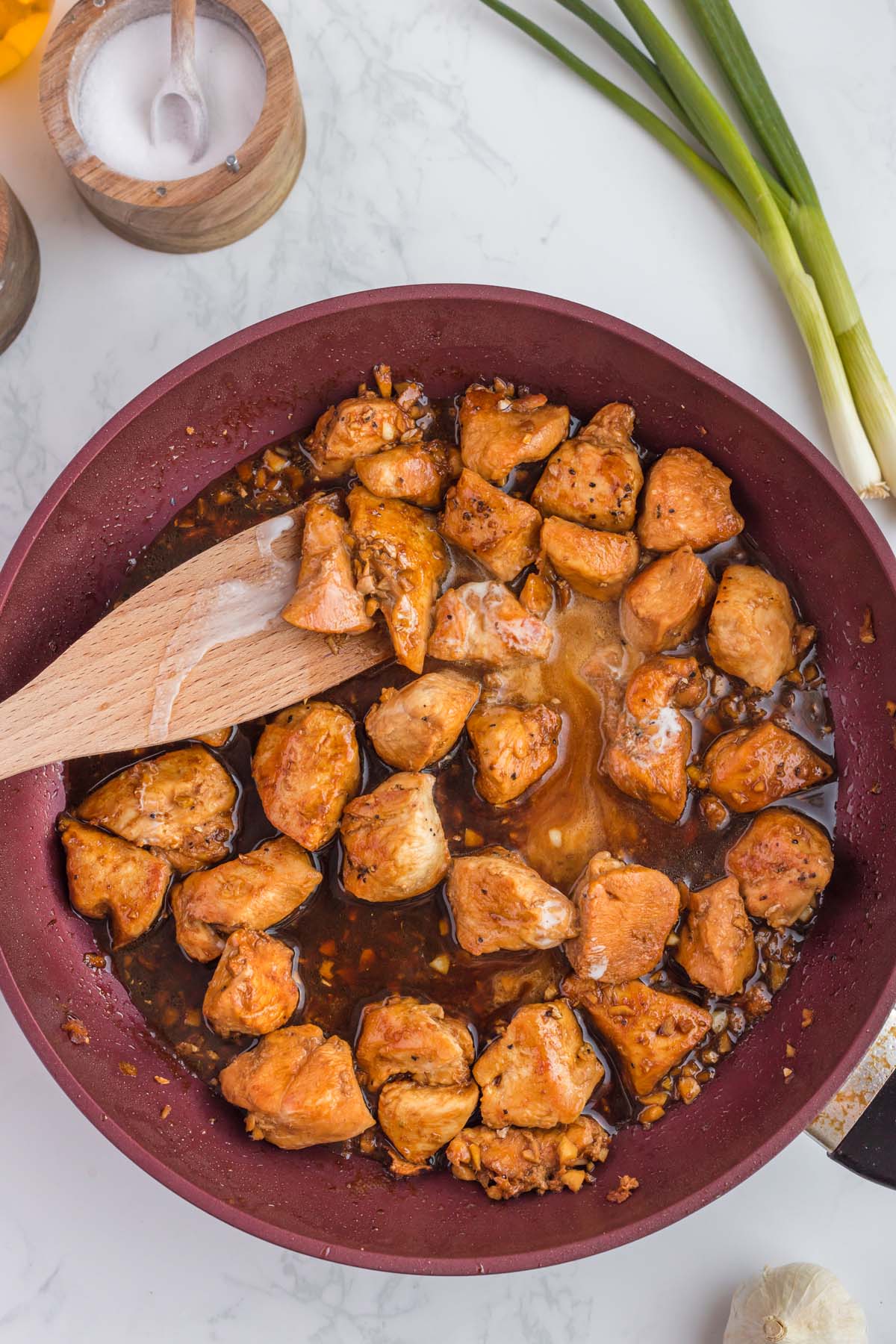 A pan of ginger chicken being mixed with a wooden spoon on a white background