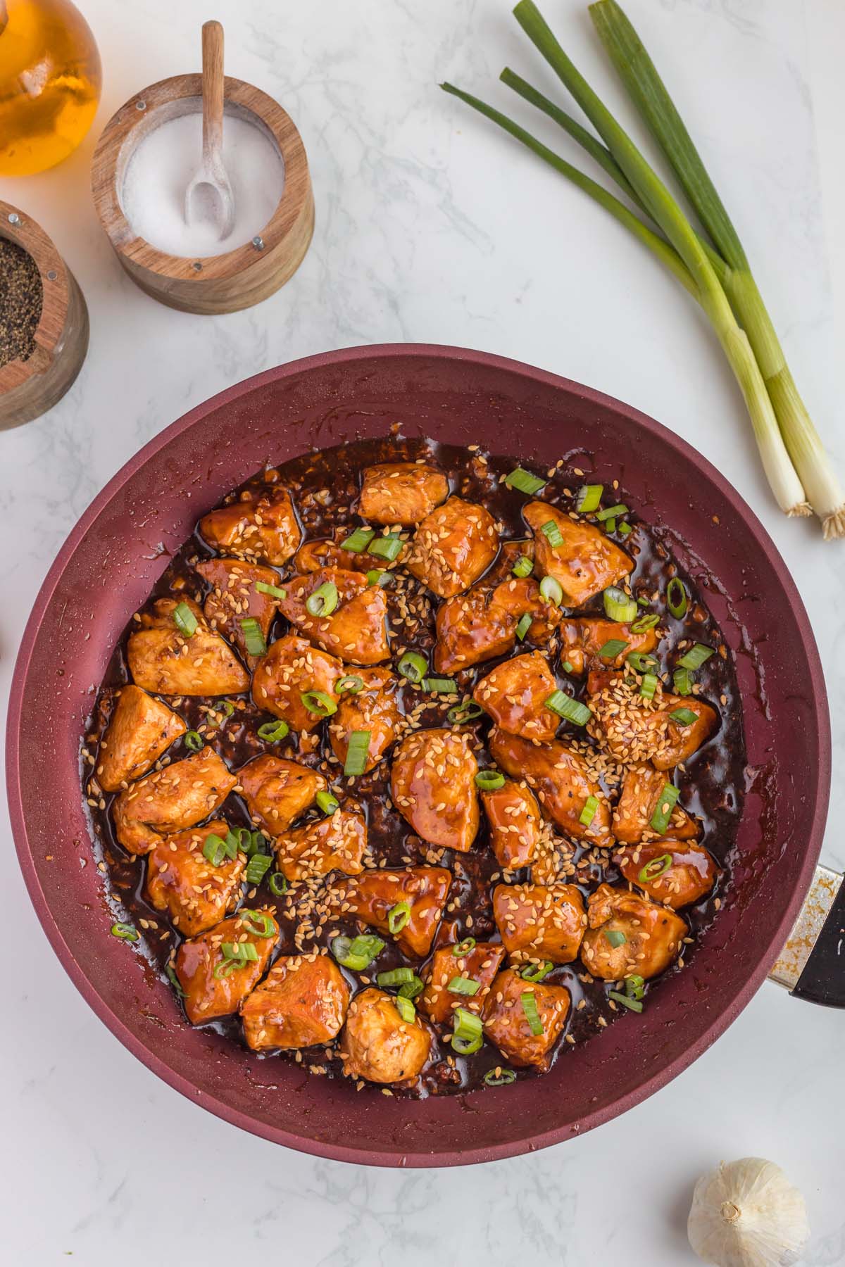 Ginger chicken in a pan with green onions on a white background with more ingredients on the side