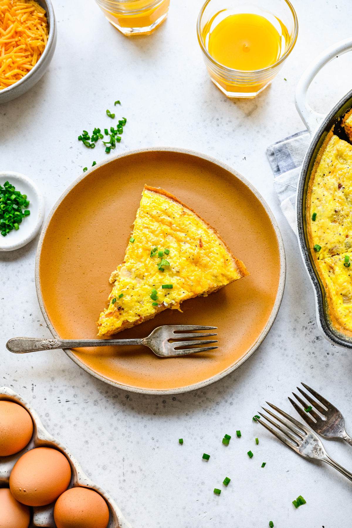 Overhead view of a plated slice of frittata sitting on a white background next to a glass of orange juice.