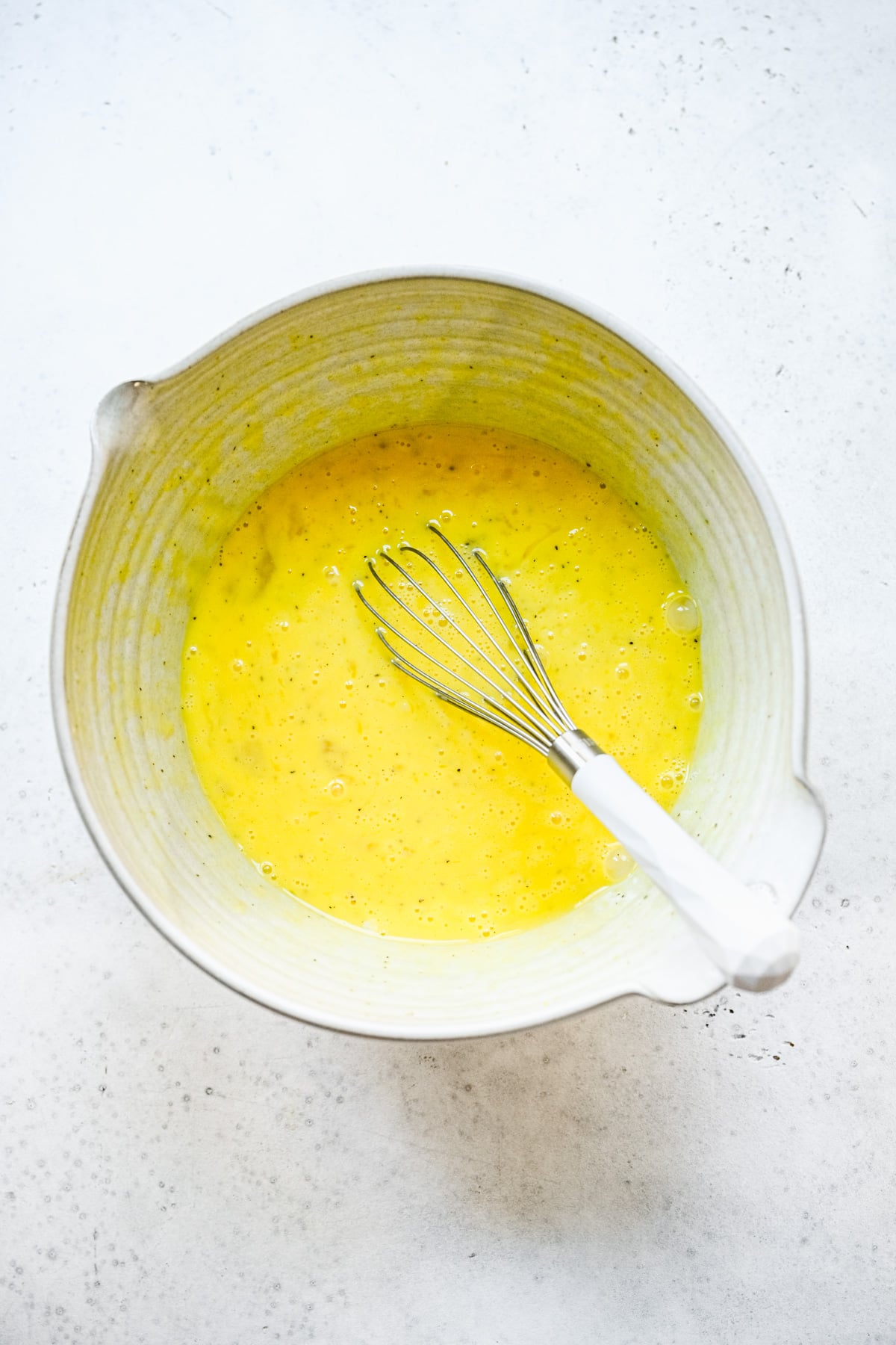 Eggs, milk, and spices being whisked in a white bowl.