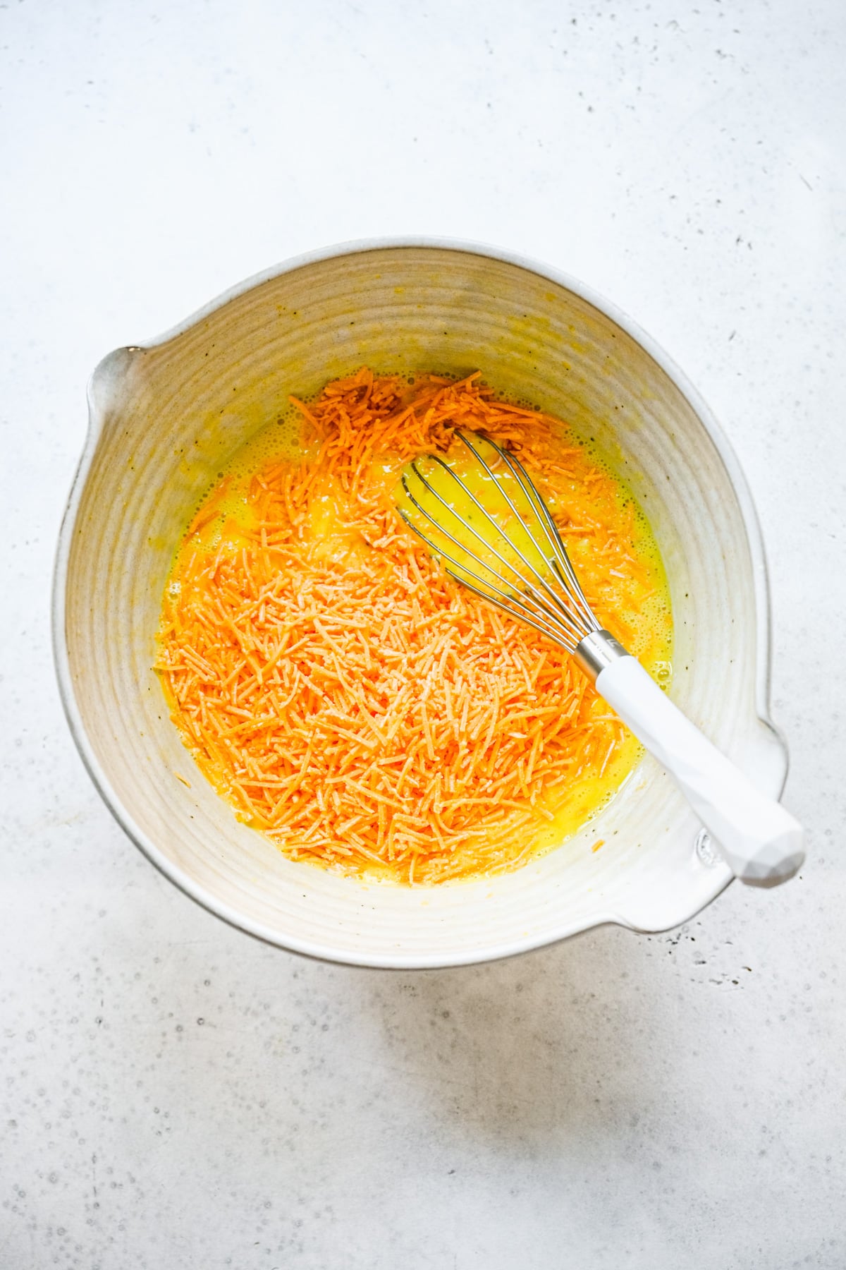 Shredded cheddar cheese being whisked into egg mixture for a keto frittata.