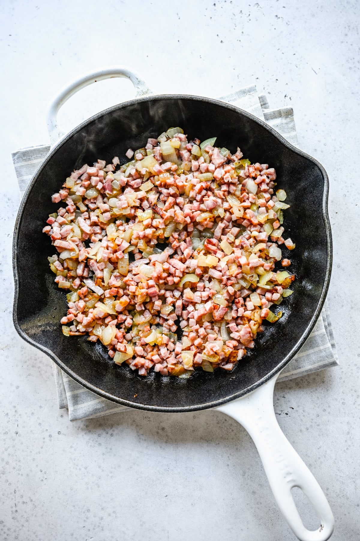 Ham and onions cooking in melted butter in a cast iron skillet, viewed from above.