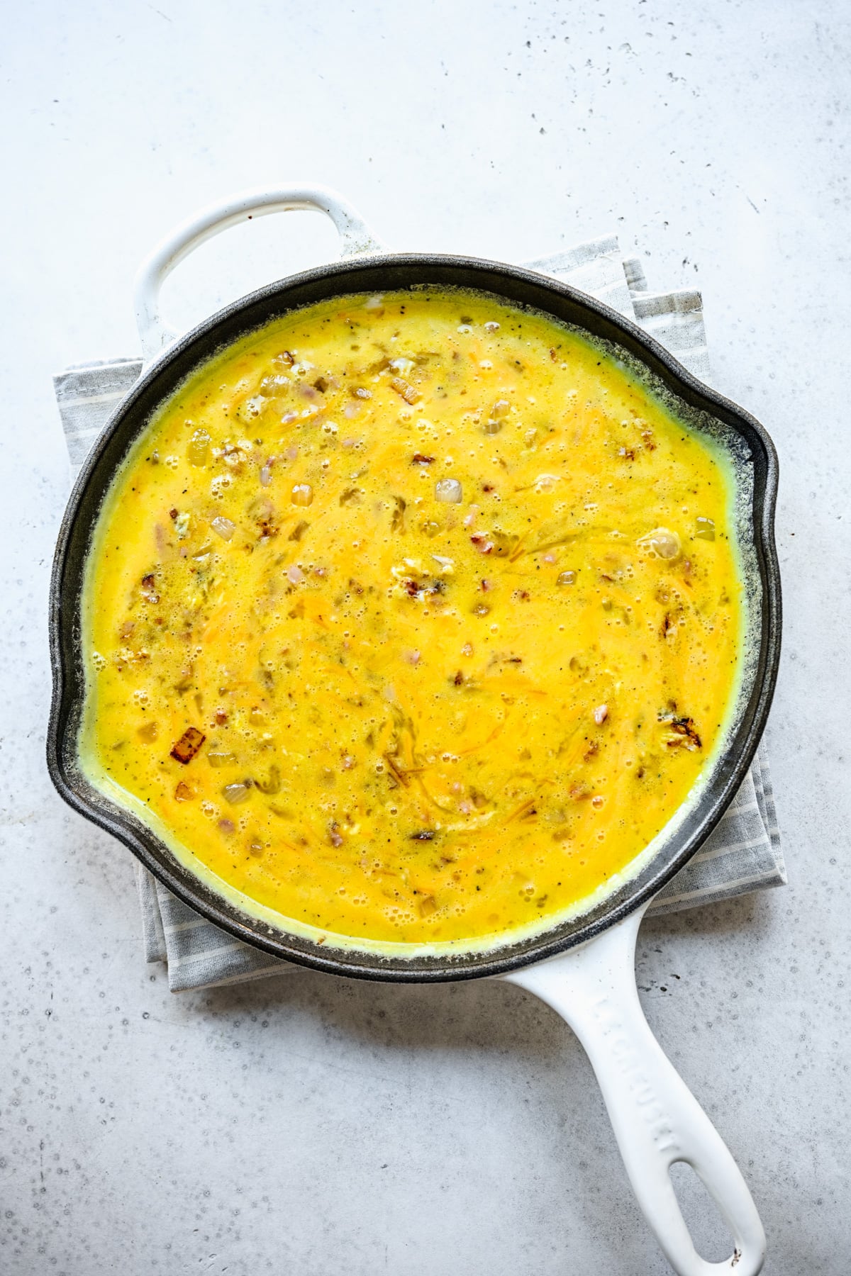 Uncooked ham and cheese frittata in a cast iron skillet, viewed from overhead.