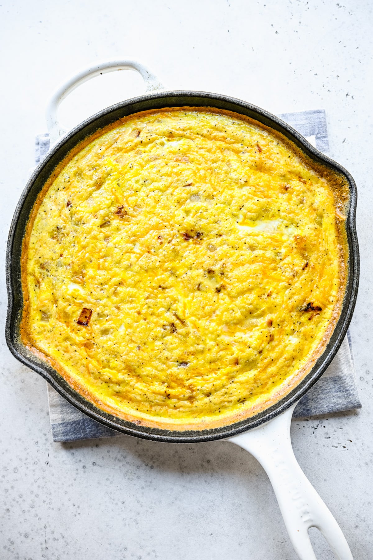 Fluffy frittata in a white skillet, viewed from overhead.