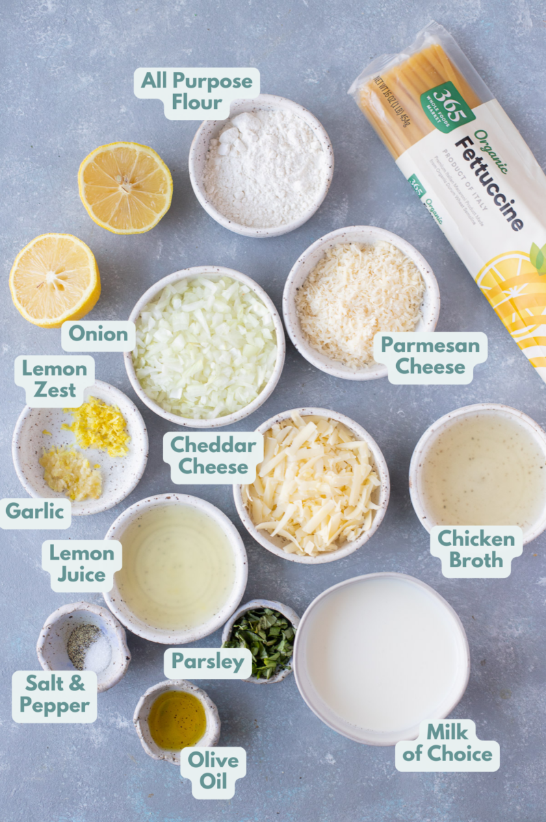 Ingredients for creamy lemon sauce in white bowls: olive oil, onions, garlic, all-purpose flour, salt, pepper, milk, cheddar cheese, parmesan cheese, chicken broth, lemon zest, lemon juice, parsley 
