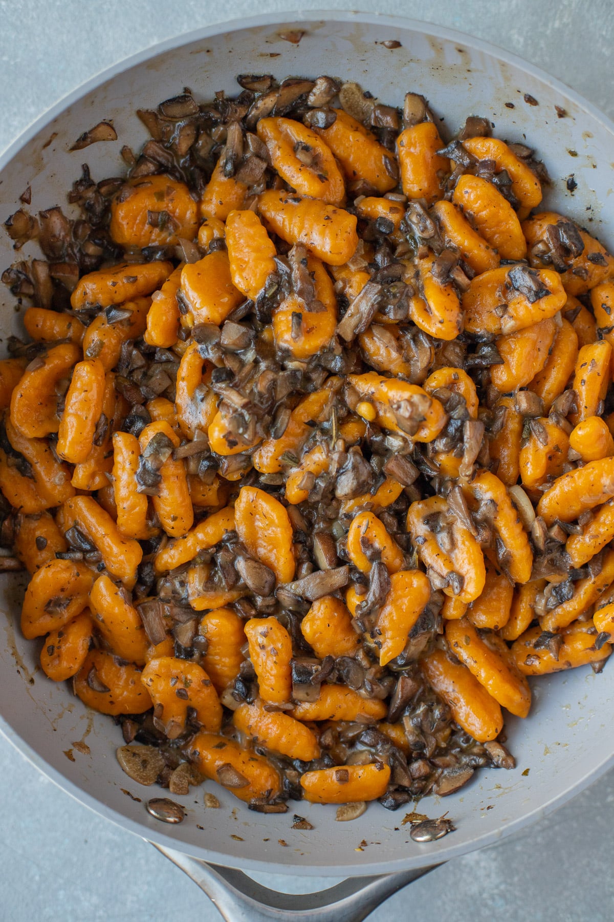 A pan of sweet potato gnocchi tossed with a gnocchi sauce on a grey background
