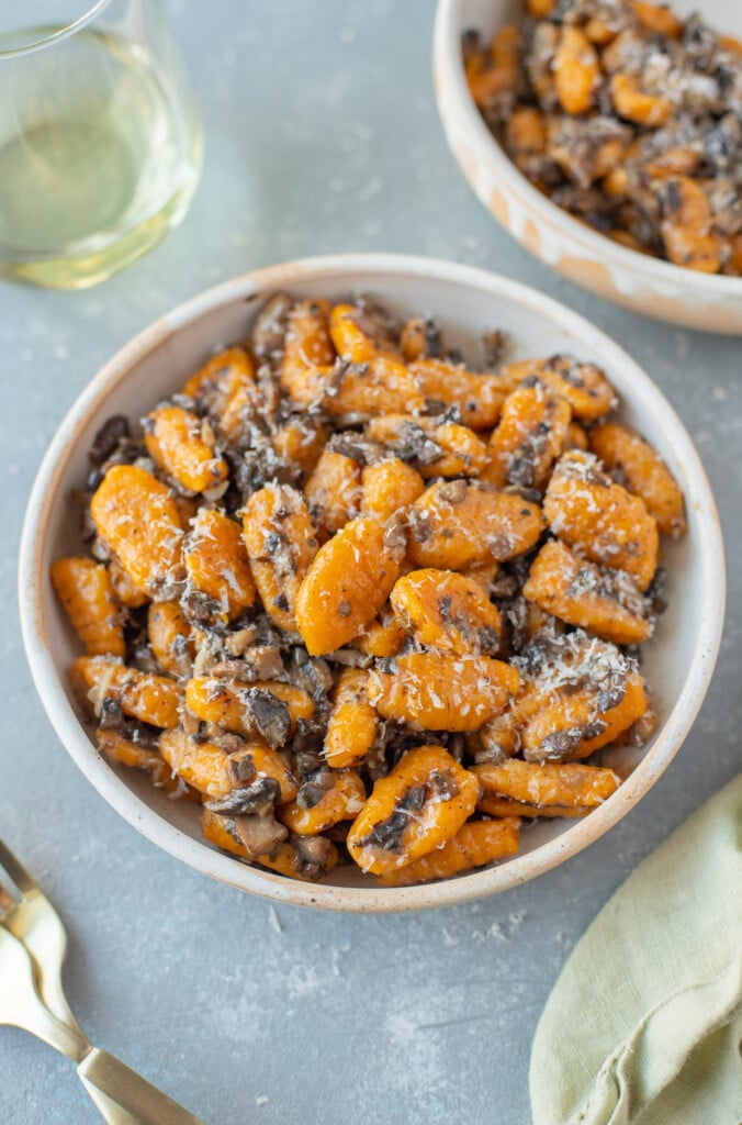 Sweet potato gnocchi in a white bowl on a grey background with another bowl and forks on the side