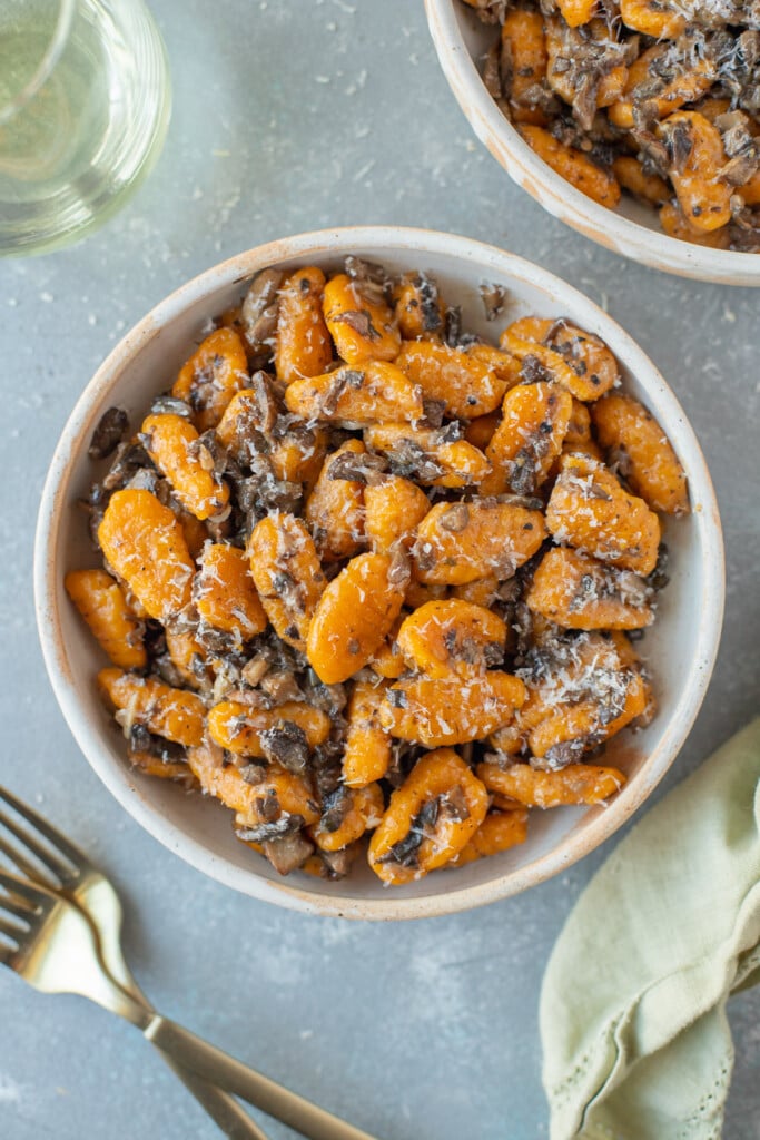 Sweet potato gnocchi in a white bowl on a grey background with another bowl and forks on the side