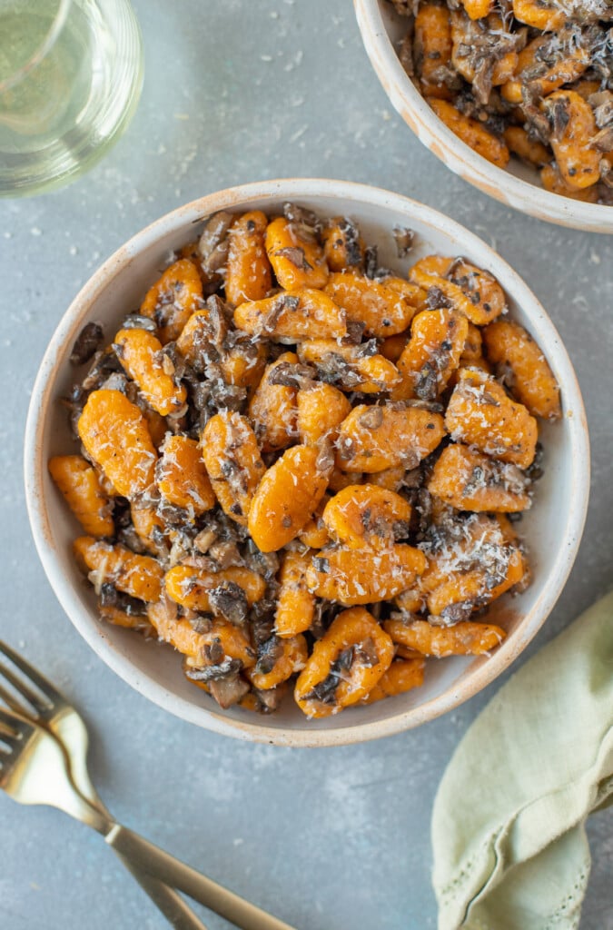 An overhead shot of sweet potato gnocchi on a grey background with another bowl and forks on the side