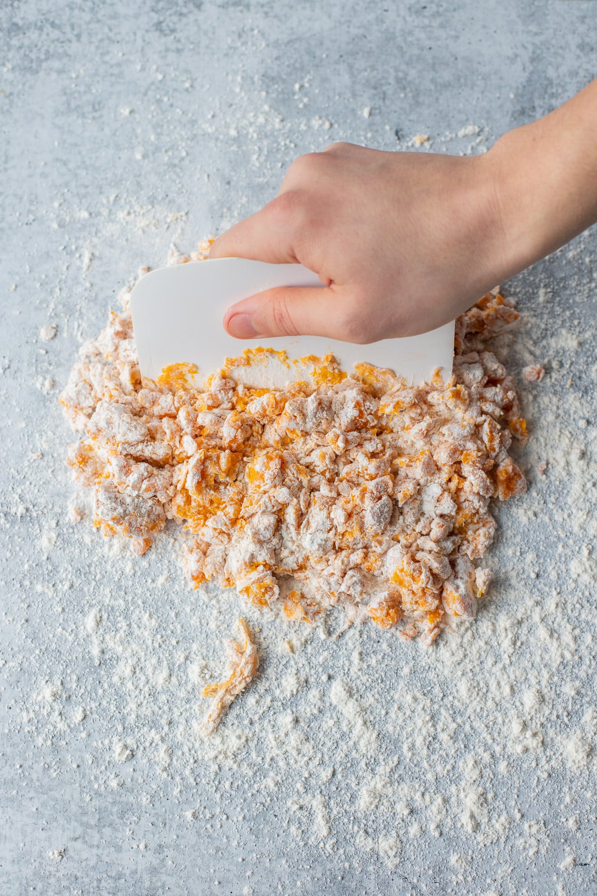 Dough for sweet potato gnocchi being mixed together with a plastic scraper on a floured counter