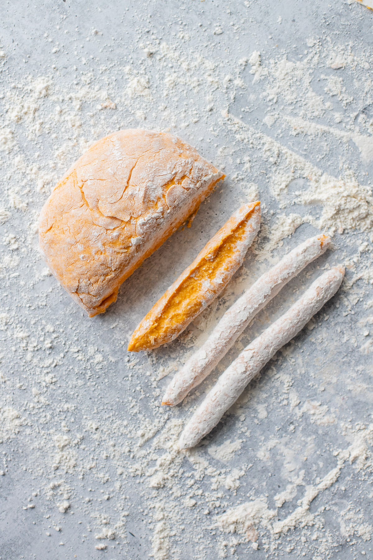 Strips being cut off a dough ball for sweet potato gnocchi on a floured surface