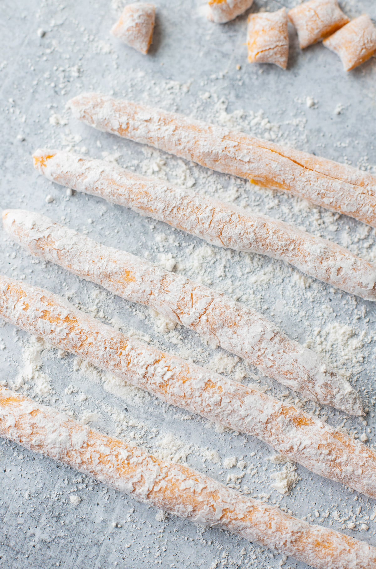 Thick sweet potato gnocchi dough ropes on a floured surface with gnocchi pieces in the background