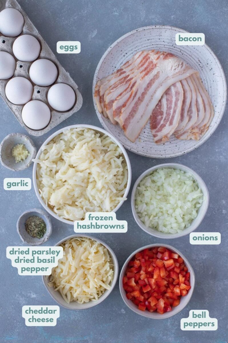Ingredients for healthy breakfast casserole with bacon in white bowls: bacon, garlic, onions, bell peppers, eggs, dried parsley, dried basil, pepper, shredded hash browns, cheddar cheese