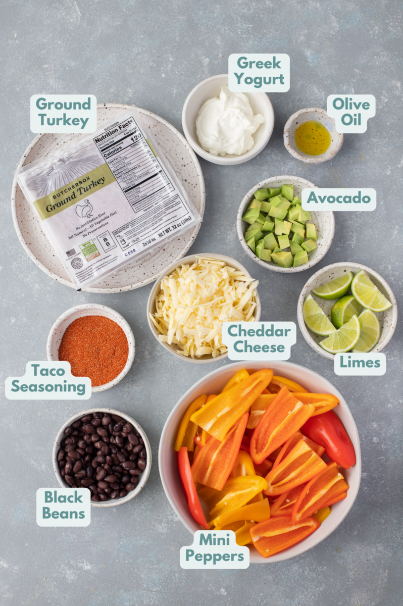 Ingredients for bell pepper nachos in white bowls: ground turkey, taco seasoning, water, mini peppers halved, black beans, cheese, greek yogurt, avocado