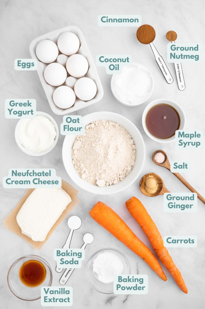 Labeled ingredients for gluten free carrot cake in bowls, measuring cups, and measuring spoons on a white background.