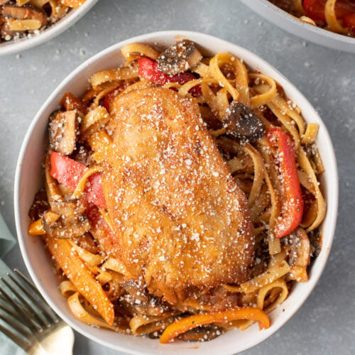 An overhead shot of chicken cacciatore in a bowl with a fork and bowl on the side