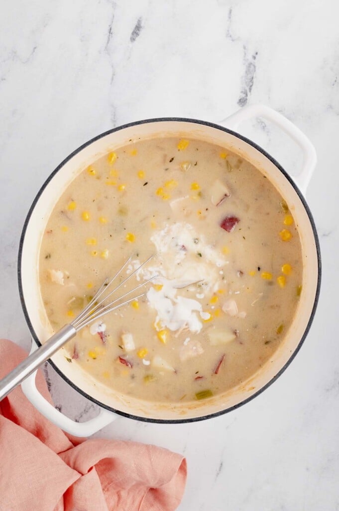greek yogurt being whisked into chicken corn chowder in a dutch oven