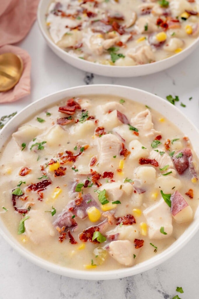 A white bowl of chicken corn chowder with another bowl in the background