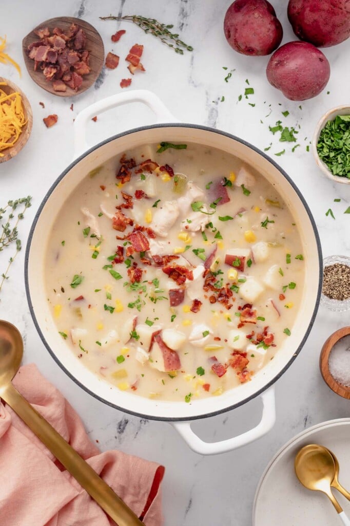 An overhead shot of a white dutch oven of chicken corn chowder with ingredients on the side