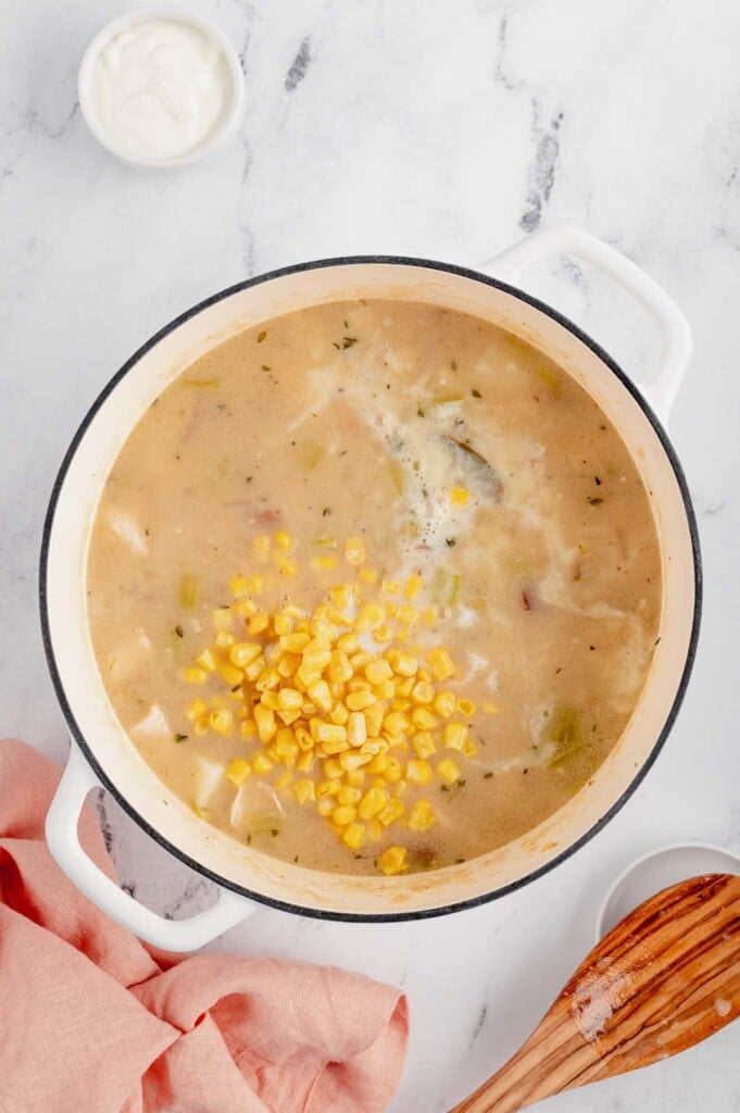 Corn and milk being added to chicken corn chowder in a dutch oven