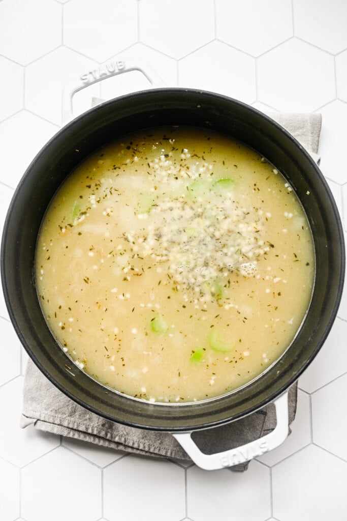 Broth, chicken and herbs added to sauteed veggies in a dutch oven to make chicken tortellini soup