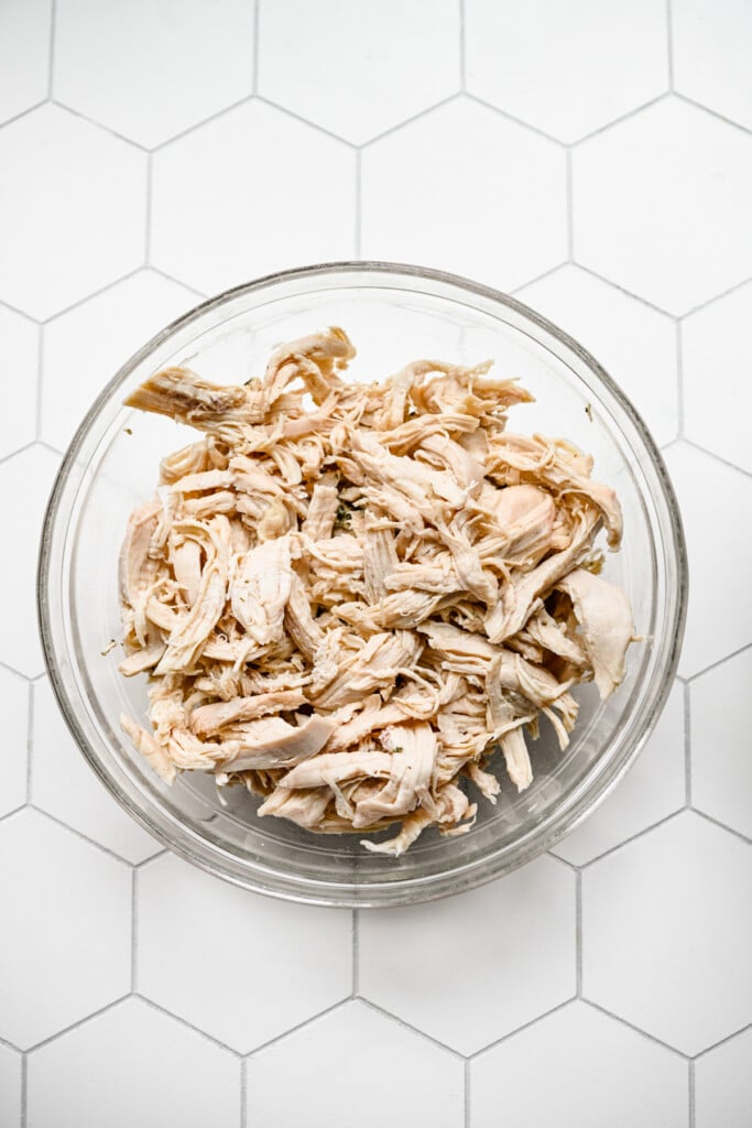 A bowl of shredded chicken to be added to chicken tortellini soup on a white background