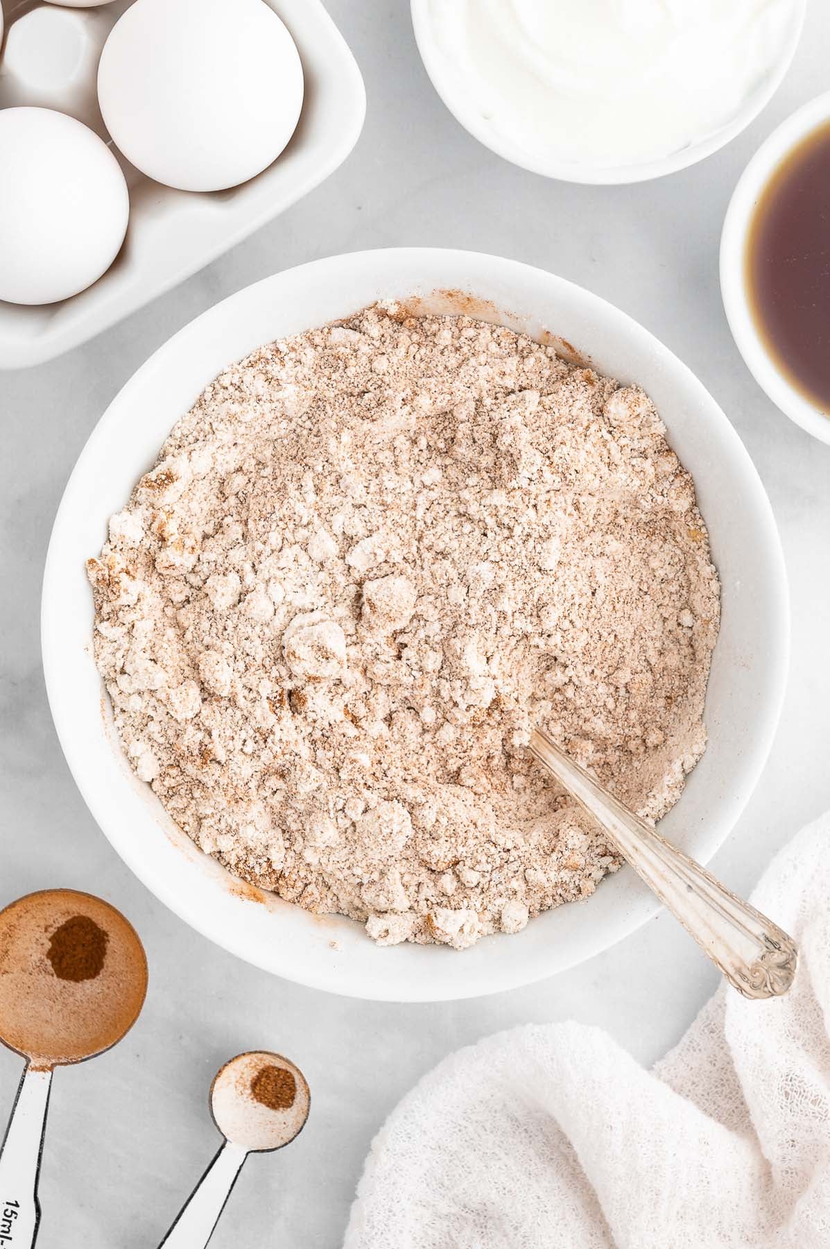Overhead view of dry baking ingredients like flour, baking soda, and spices in a large white mixing bowl.