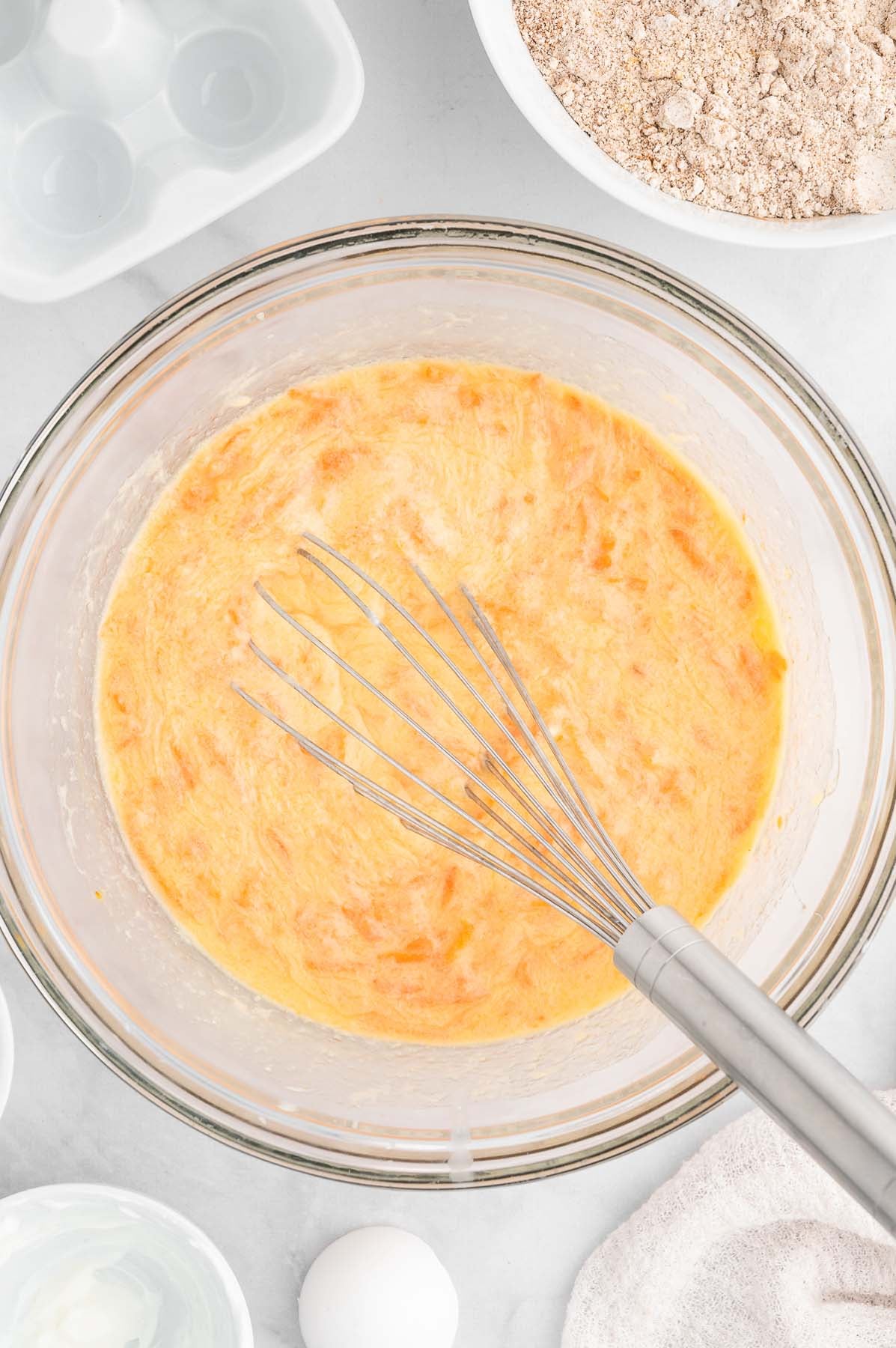 Overhead view of yellow batter in a clear glass mixing bowl with a wire whisk.