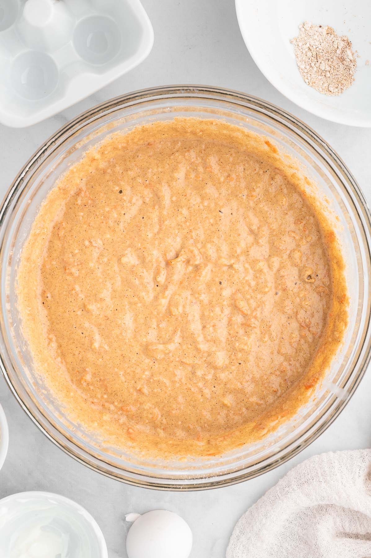Healthy carrot cake batter in a large glass mixing bowl, viewed from overhead.