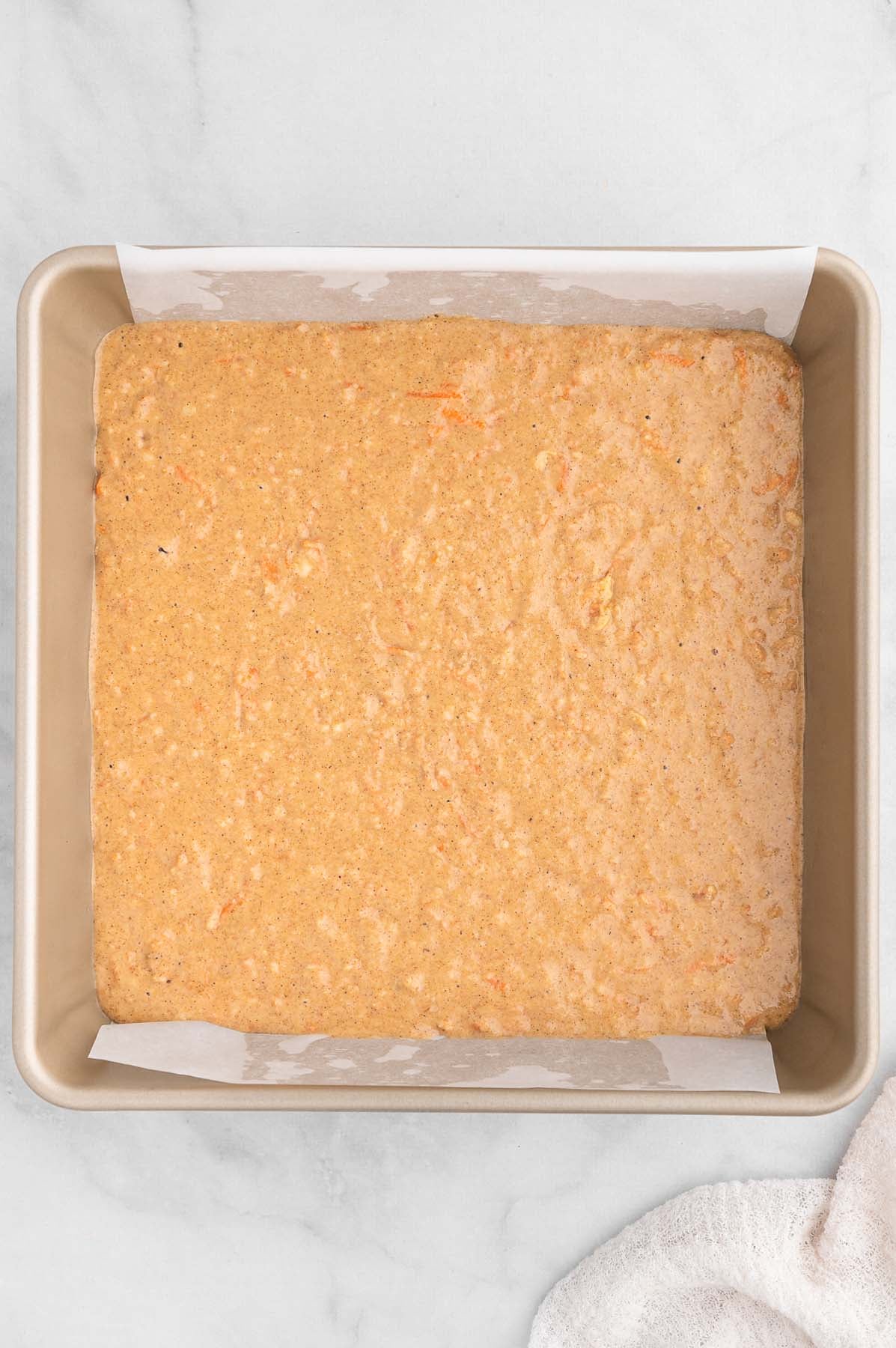Unbaked gluten free carrot cake batter in a square baking pan, viewed from overhead.