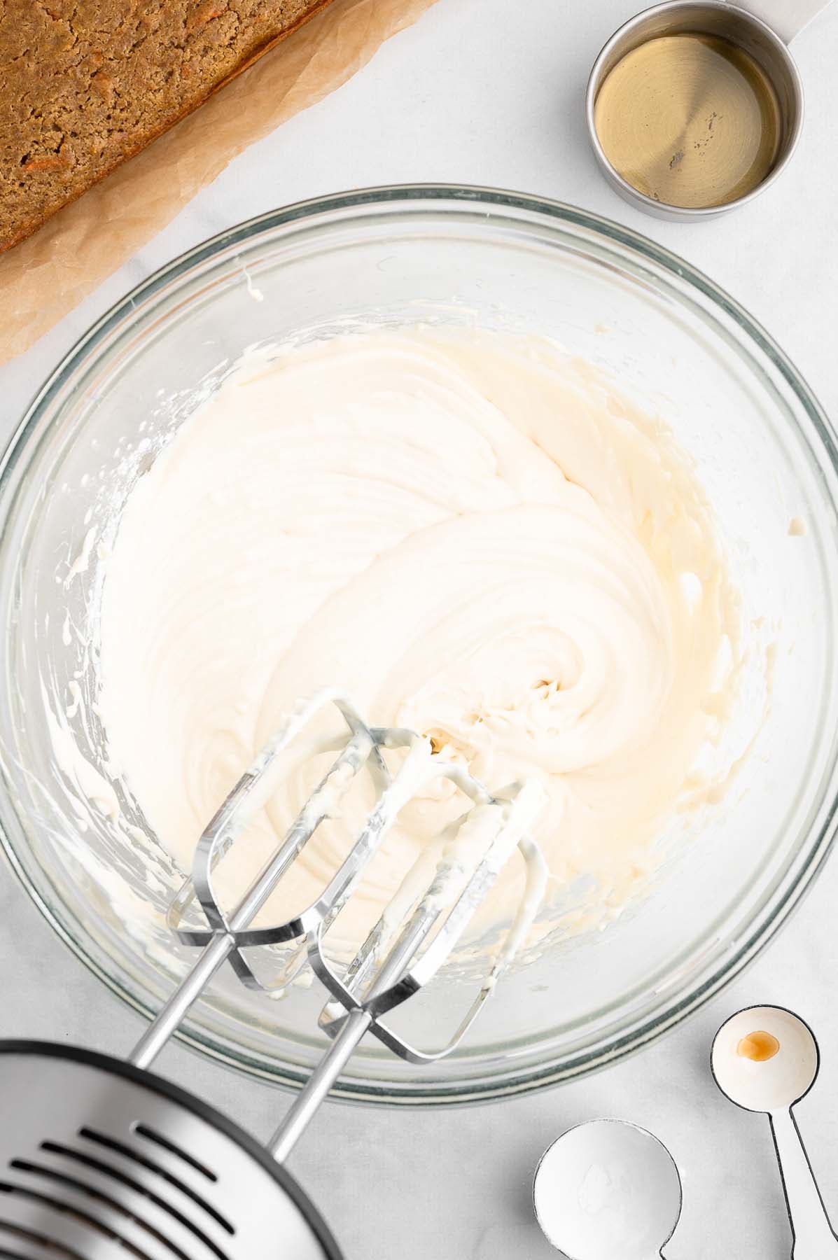 Electric handheld mixer in a bowl of cream cheese frosting, viewed from above.