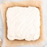 An overhead shot of a healthy carrot cake frosted with a healthy cream cheese frosting on a piece of parchment paper