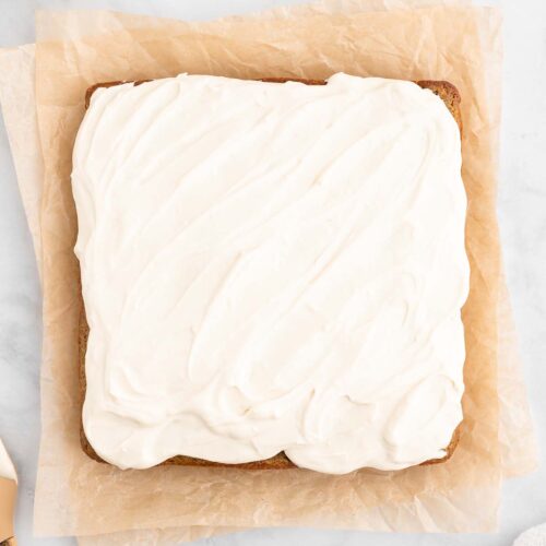 An overhead shot of a healthy carrot cake frosted with a healthy cream cheese frosting on a piece of parchment paper