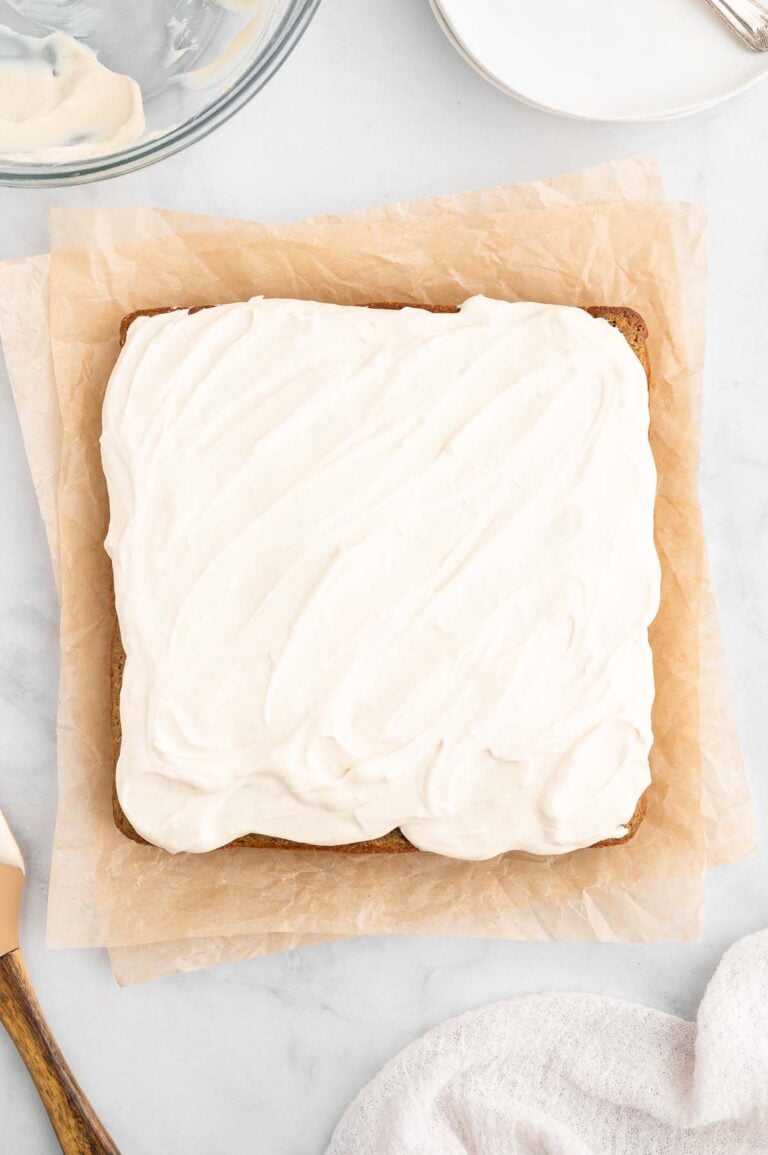 An overhead shot of a healthy carrot cake frosted with a healthy cream cheese frosting on a piece of parchment paper
