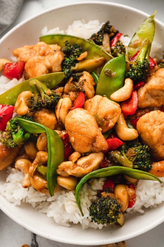 A close up of cashew chicken on a bed of white rice on a white plate