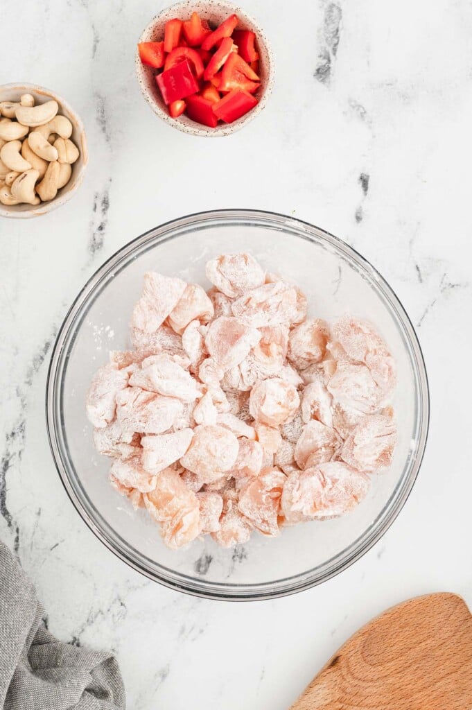 Chicken pieces in a clear bowl seasoned with salt, pepper, and cornstarch  on a marble background