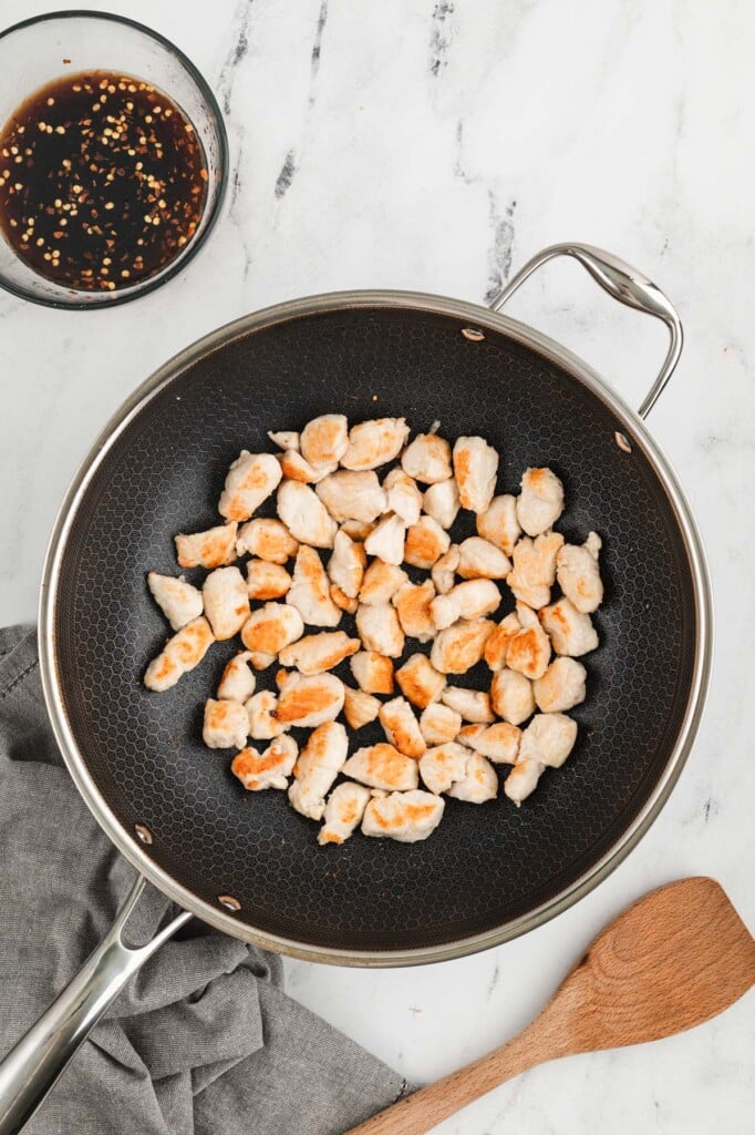 An overhead shot of cooked chicken pieces in a large wok with cashew chicken sauce on the side