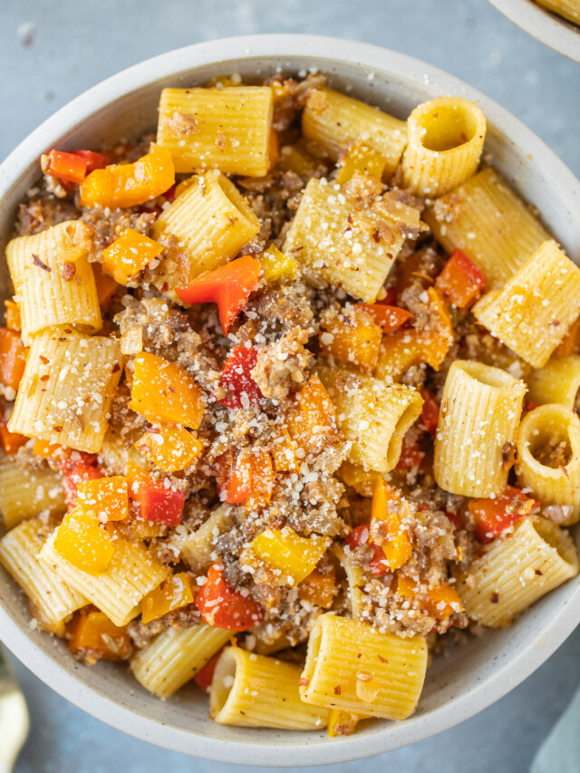 An overhead shot of a bowl of sausage and peppers pasta on a grey background