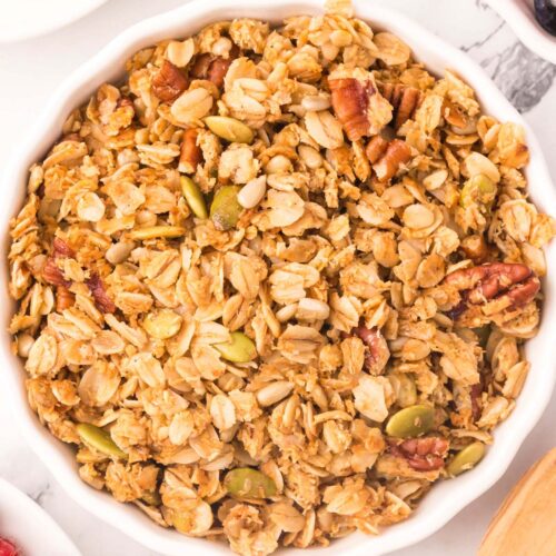 A white bowl of homemade granola on a white background