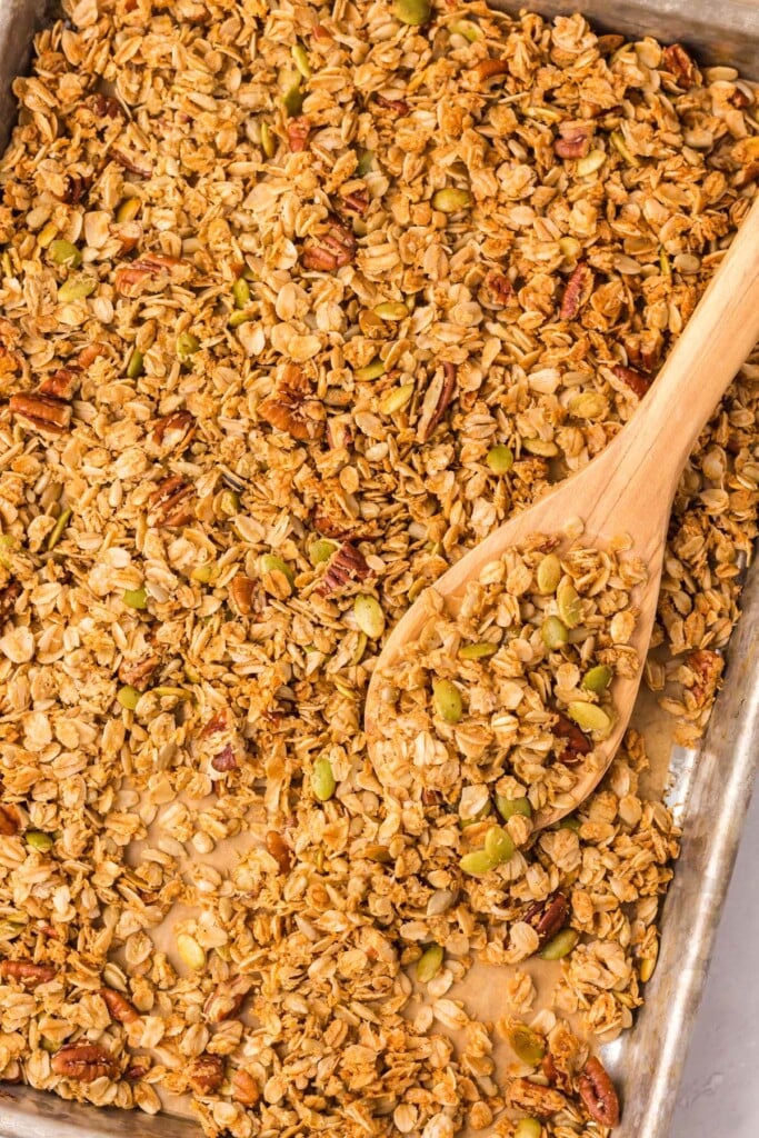 Simple granola on a baking sheet with a wooden spoon on it