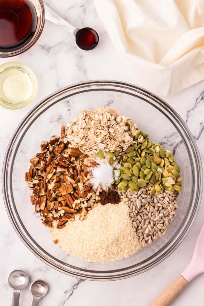 rolled oats, coconut, sunflower seeds, pepitas, chopped pecans, salt and vanilla powder in a clear bowl before being combined to make homemade granola