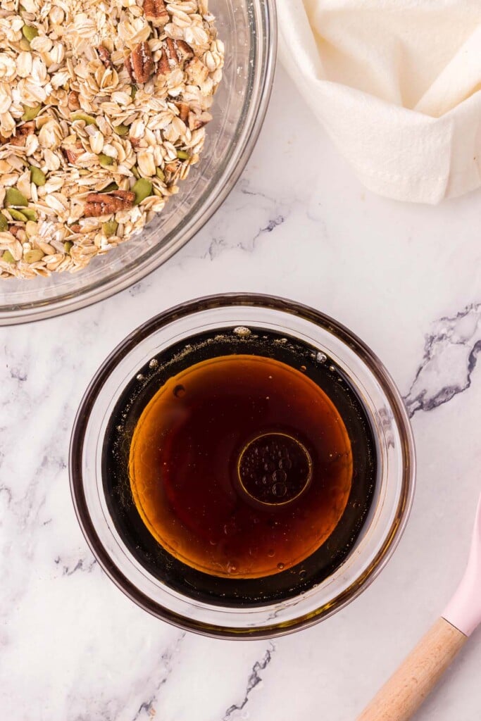 maple syrup, oil, and vanilla in a clear bowl before being added to dry ingredients for homemade granola on the side