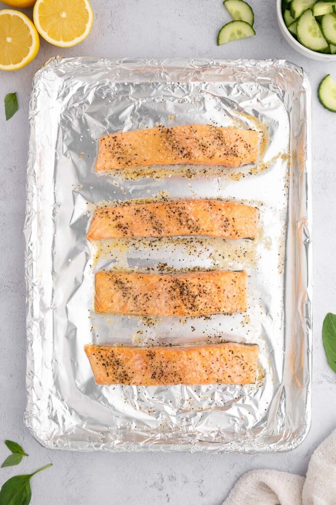 Four salmon filets on a foil lined baking sheet brushed with oil and lemon juice and topped with garlic powder, salt and pepper before baking