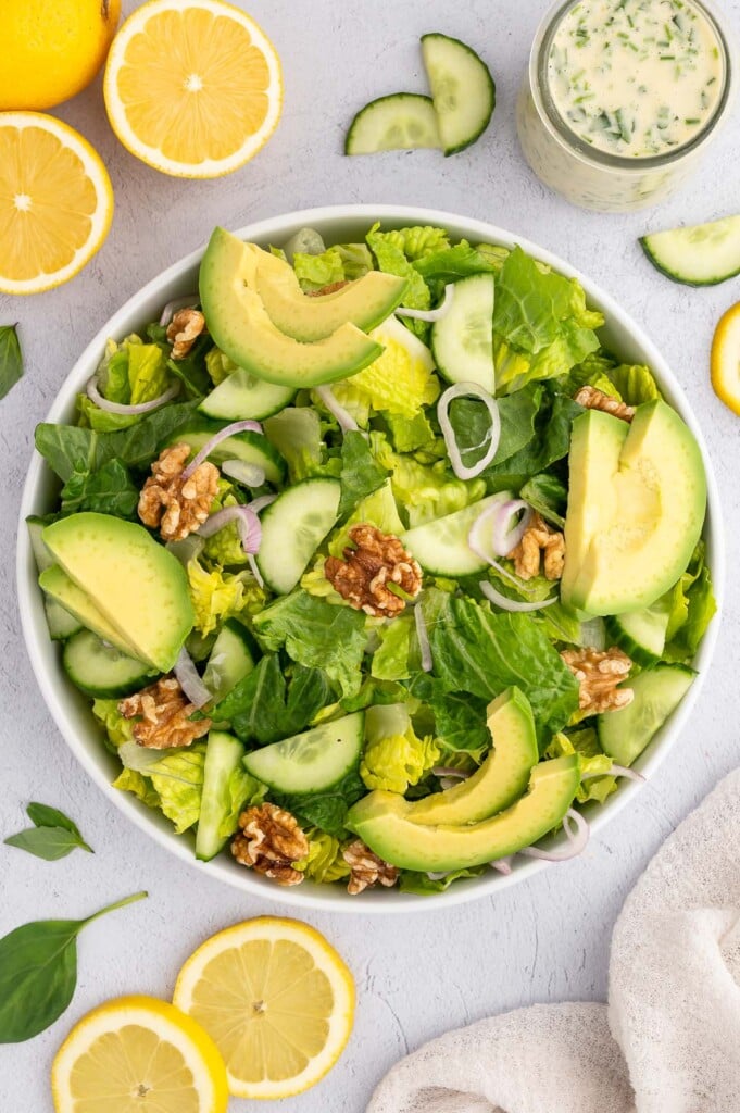 An overhead shot of a large bowl with romaine lettuce, avocados, cucumber, shallots, and walnuts on top