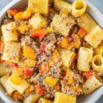 An overhead shot of a bowl of sausage and peppers pasta on a grey background