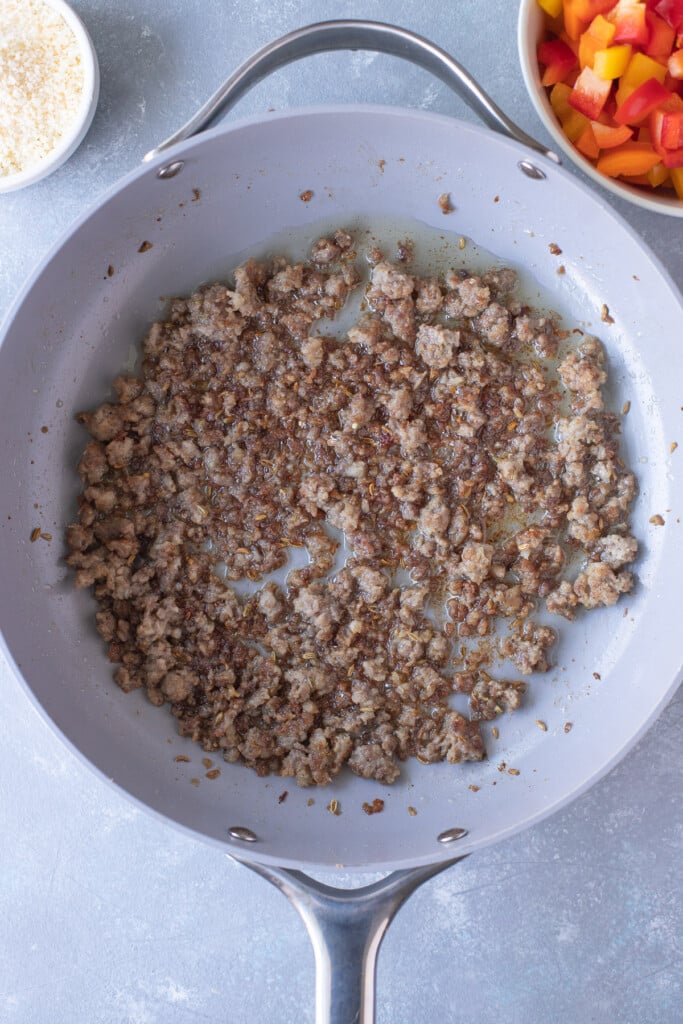 Ground sausage in a pan after being browned and broken up with peppers on the side