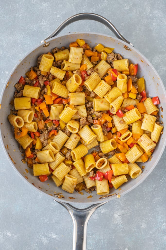 Pasta tossed with sausage and peppers in a skillet on a grey background